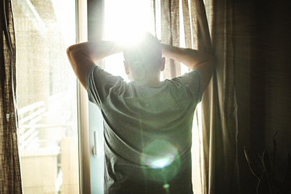 Rear view of adult man looking through window in bedroom
